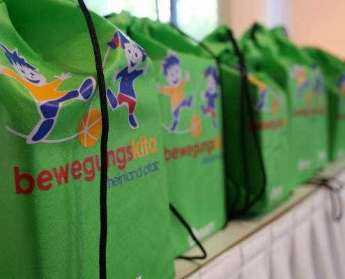 Mehrere grüne Turnbeutel nebeneinander mit der Aufschrift Bewegungskita Rheinland-Pfalz