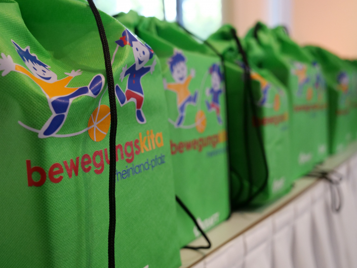 20 Jahre Verein Bewegungskita2 Mehrere grüne Turnbeutel nebeneinander mit der Aufschrift Bewegungskita Rheinland-Pfalz
