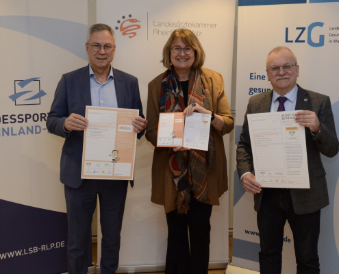 Drei Personen stehen nebeneinander und halten Dokumente in die Kamera